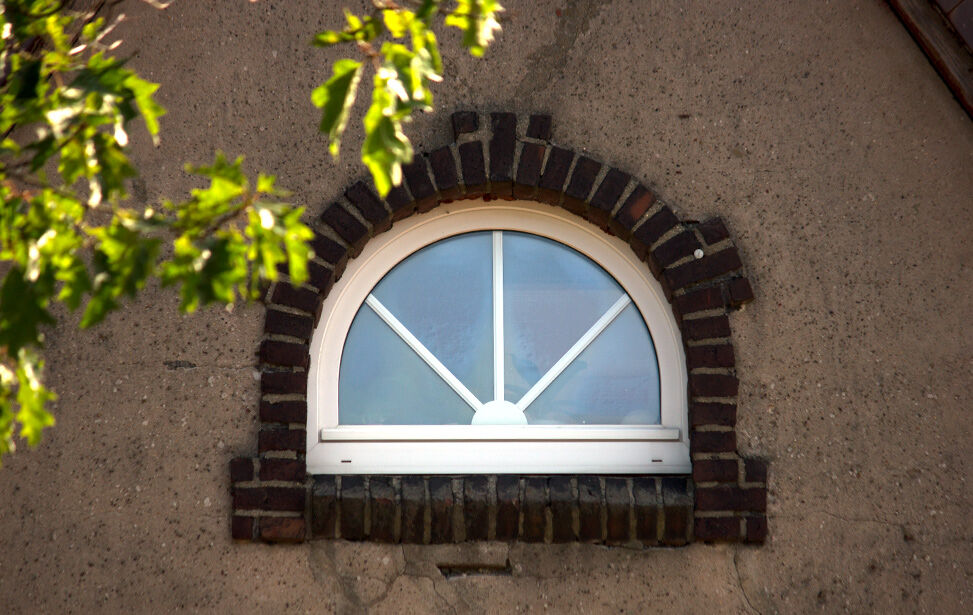 Rundbogenfenster mit weißem Rahmen in einer Klinkerfassade