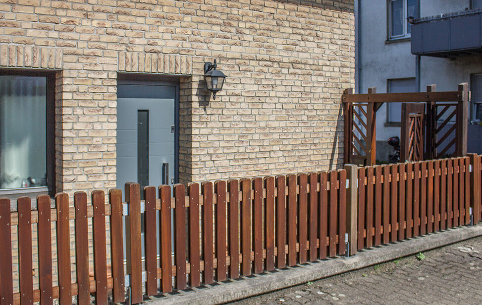 Holzzaun mit Tor vor einer Klinkerfassade